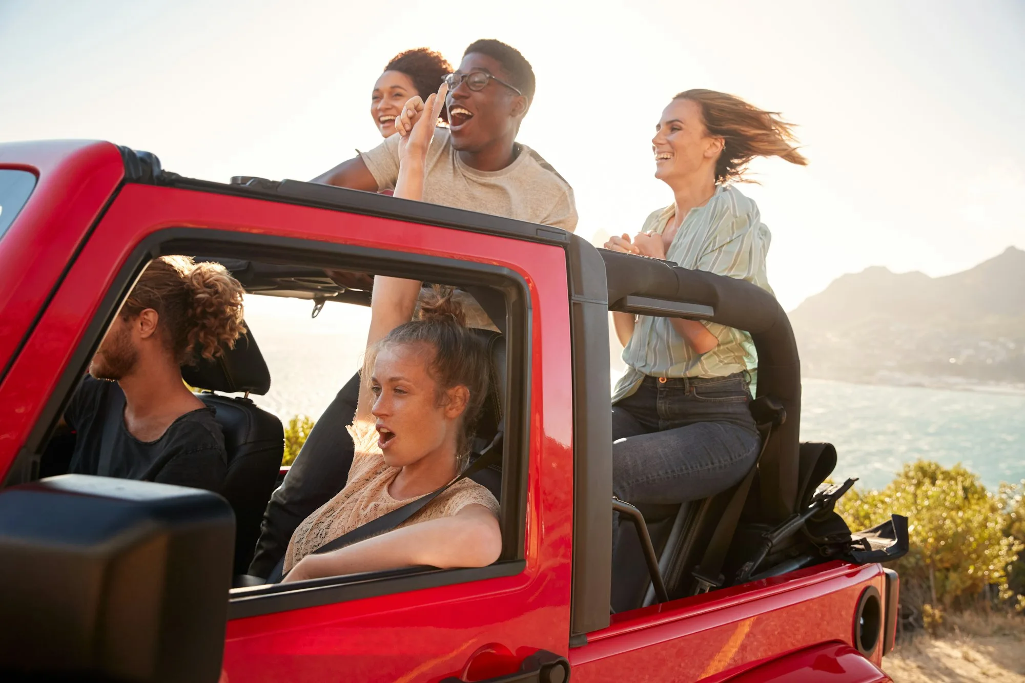 Five young adult friends on a road trip driving in an open top jeep by the sea