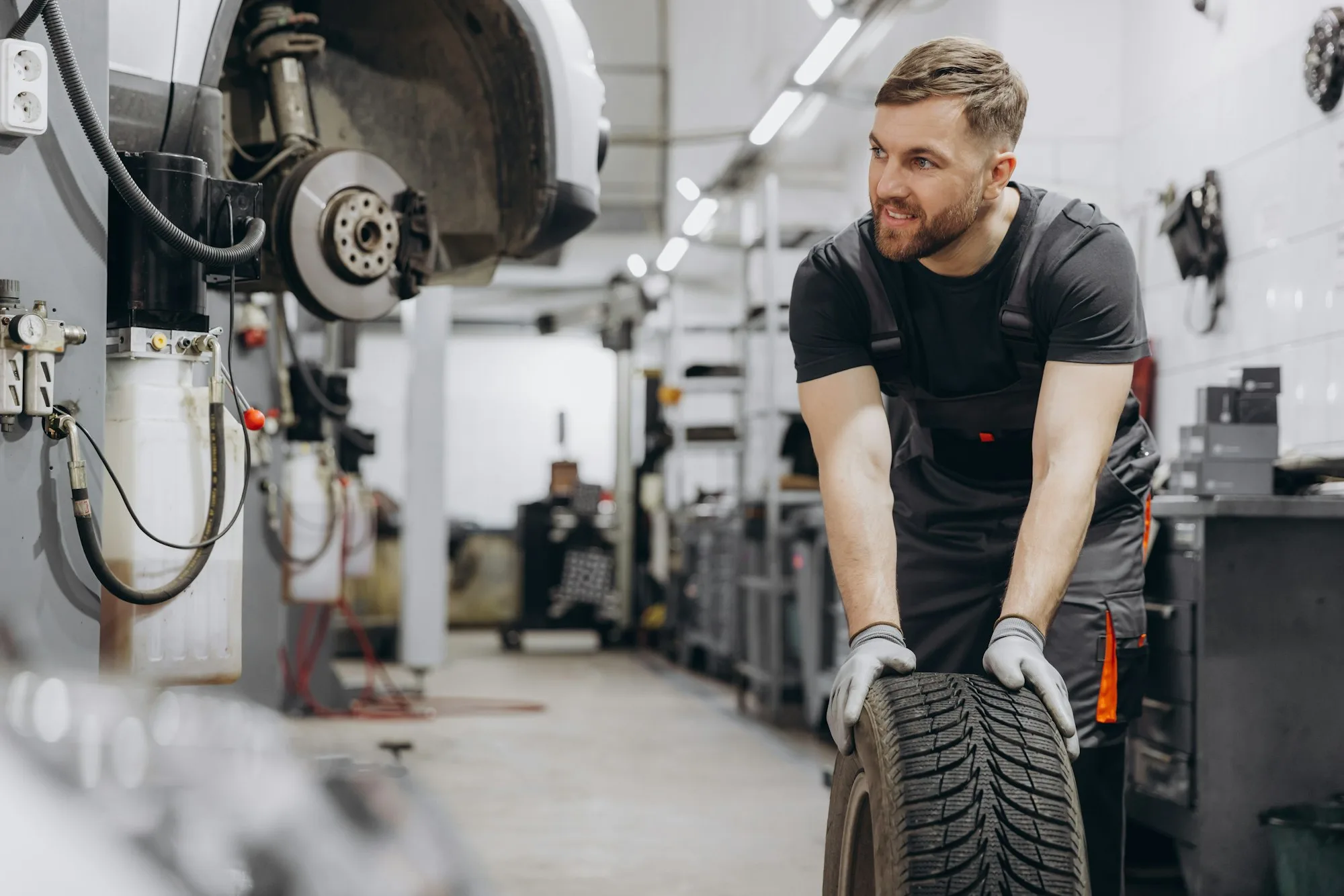 Happy Smiling Car mechanic working in garage and changing wheel alloy tire