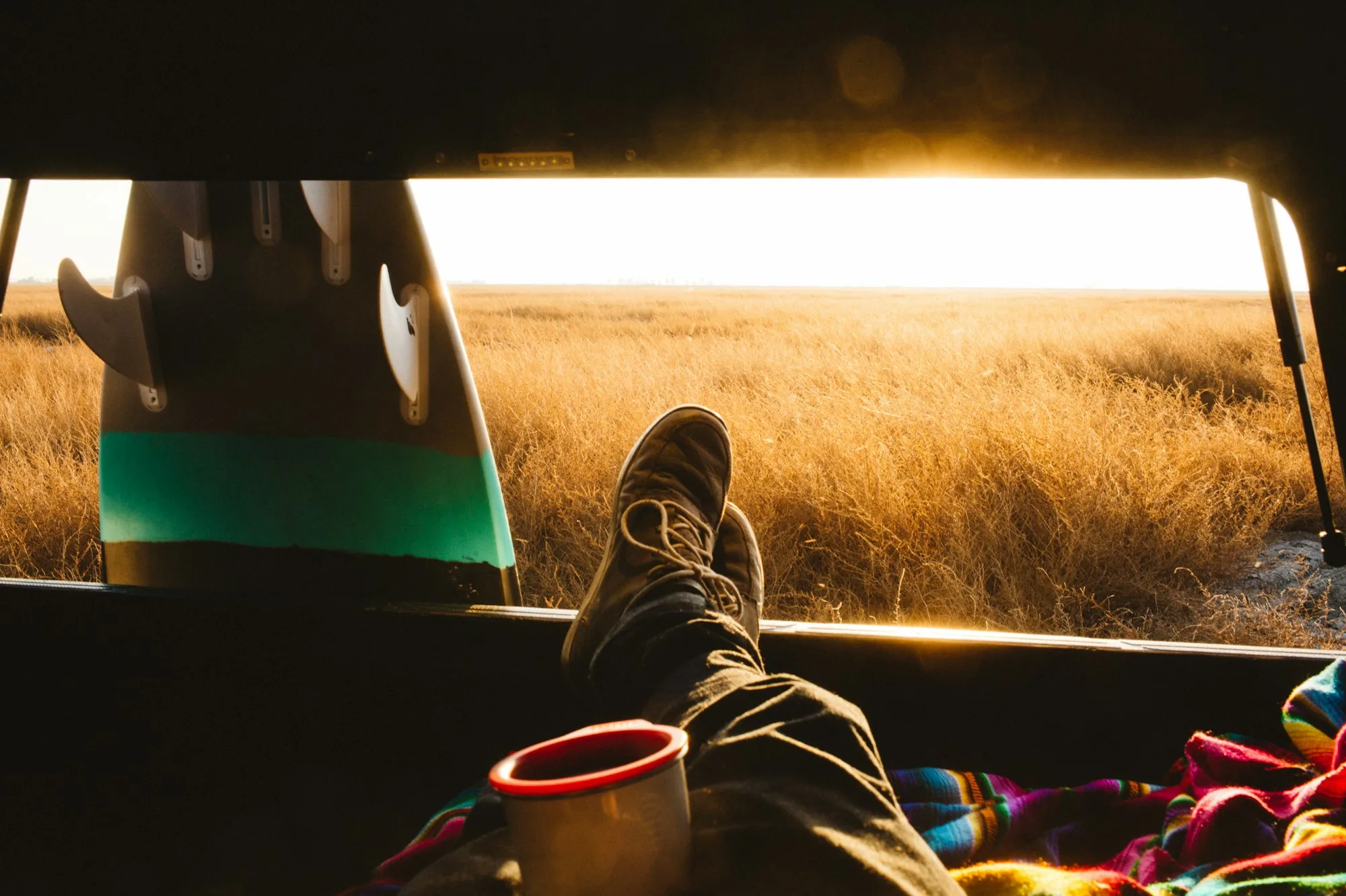 Male surfer with feet up in back of jeep at sunset, San Luis Obispo, California, USA